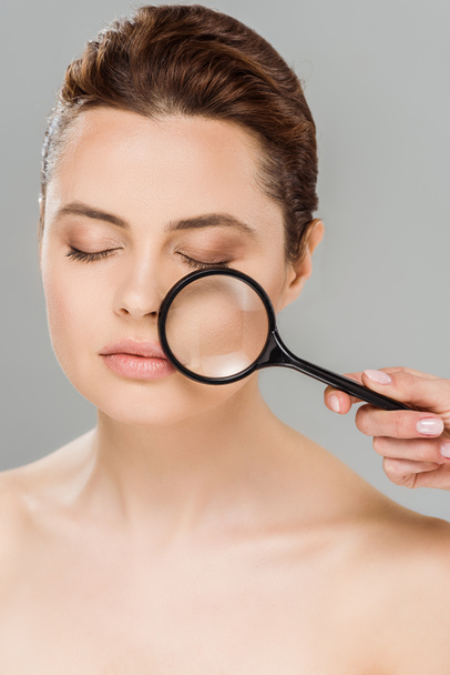 naked woman with closed eyes holding magnifying glass near face isolated on grey  - Foto, Bild