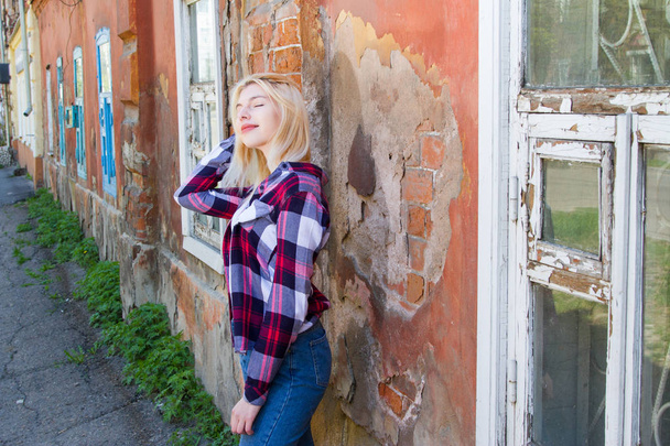 Mädchen in Jeans und kariertem Hemd steht am alten baufälligen Haus - Foto, Bild