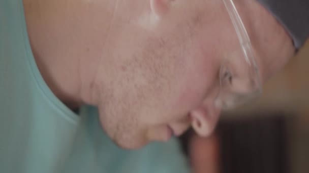 Κοντινό πορτρέτο του νεαρού Μάστερ μηχανικός σε unifrom γυαλιά επικεντρώθηκε στην διάτρηση μια τρύπα με διάτρηση - Πλάνα, βίντεο