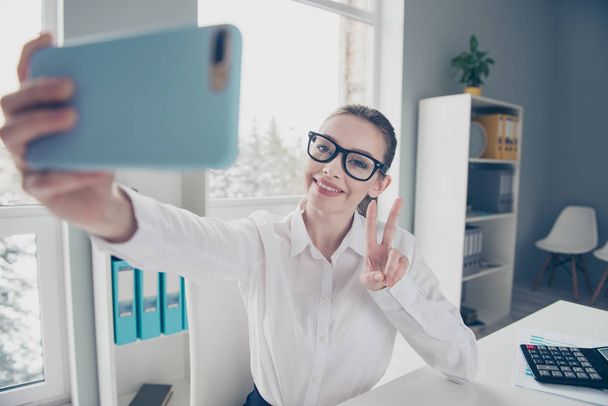 Close up photo beautiful she her business lady eyewear eyeglasses hands arms telephone v-sign friendly toothy say hi colleagues sit table wear specs formal-wear white shirt modern bright office - Фото, зображення
