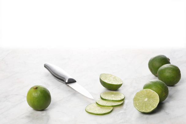 whole and slices lime fruits with a knife on a marble table, white background and copy space for your text - Photo, Image
