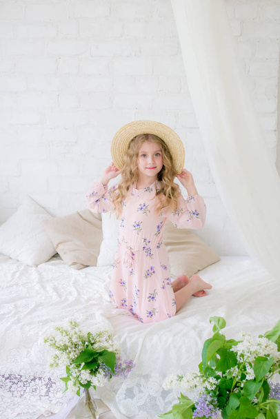 Cute little girl with blond hair in a beautiful dress in a spring studio with lilac flowers - Foto, afbeelding