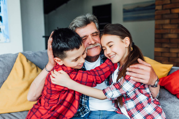 Grandfather with children smiling, sitting on couch and hugging - Foto, imagen