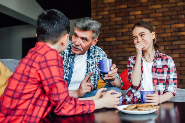 smiling grandfather with children drinking tea with cookies  - Photo, image