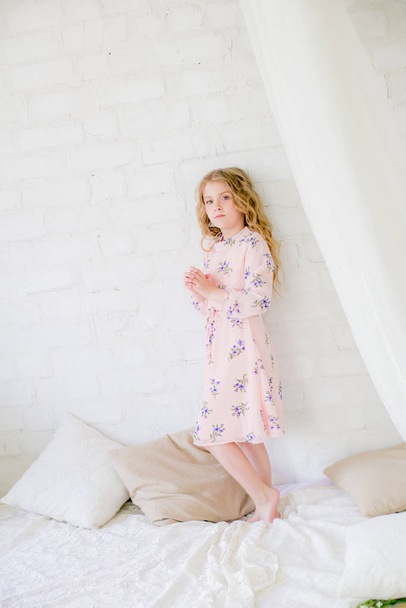 Cute little girl with blond hair in a beautiful dress in a spring studio with lilac flowers - Foto, Imagem