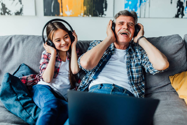 Happy grandfather with girl listening music in headphones while lying at home - Foto, Imagem