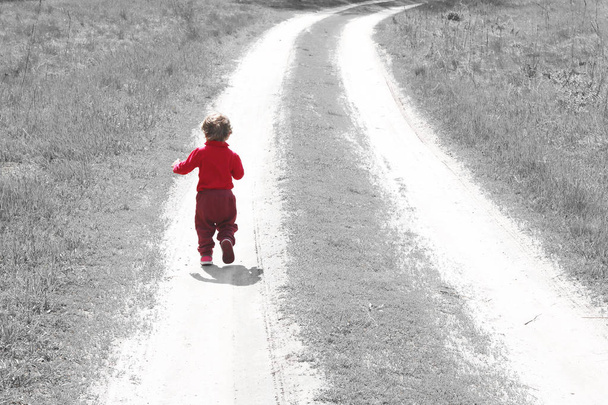 Abstract photo with small child in red clothes from back, who runs off into distance along road among grass as symbol of growing children and desire of children to become adult - Photo, Image