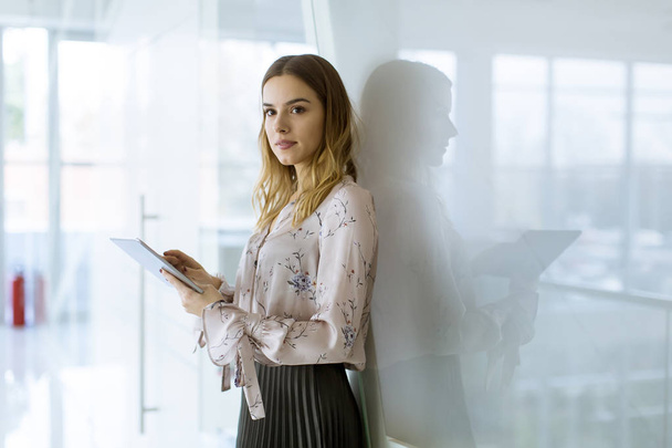 Vonzó fiatal üzletasszony segítségével digitális tabletta állva az irodában - Fotó, kép