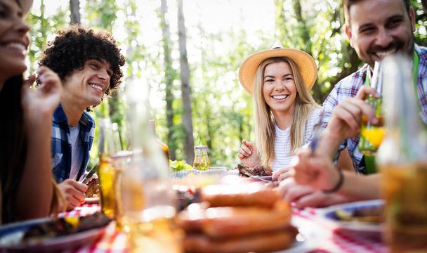 Group of happy friends eating and drinking beers at barbecue dinner outdoors - Photo, Image