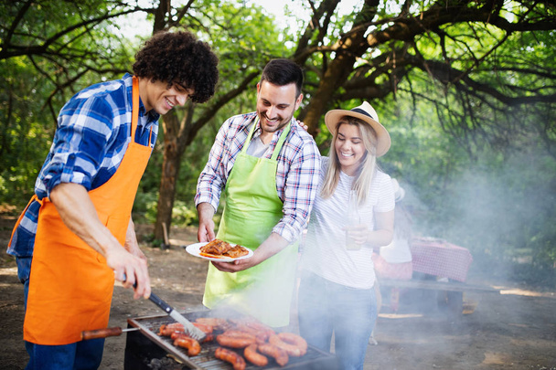 Young female and male couple baking barbecue in nature with friends - Photo, image
