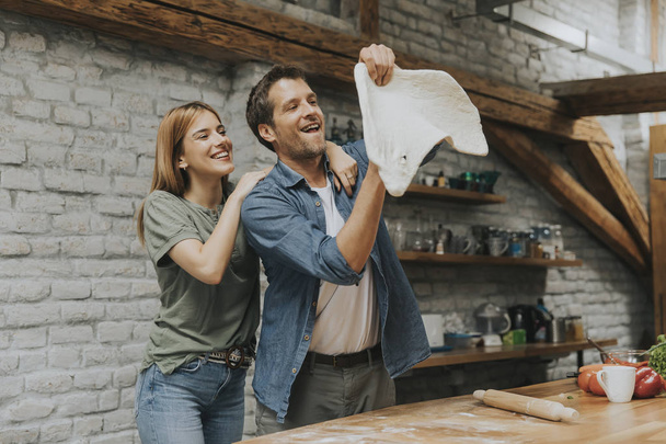 Young couple caking pizza in rustic kitchen together - Foto, Bild