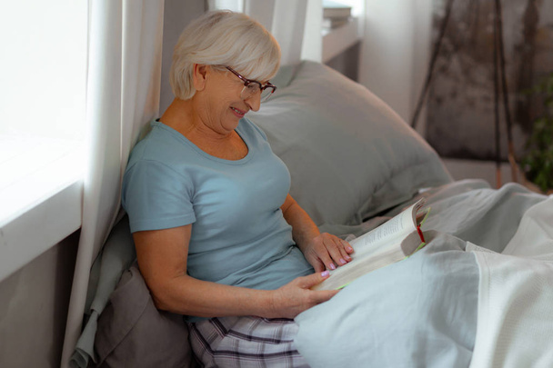 Smiling beaming dame happily reading a book in the bed. - Foto, Imagem