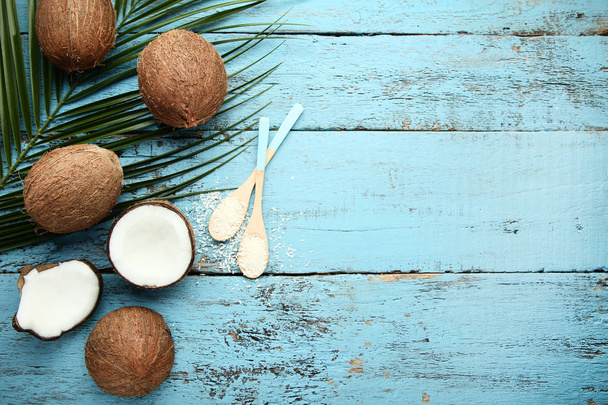 Ripe coconuts with flakes in spoons and palm leafs on blue woode - Fotografie, Obrázek