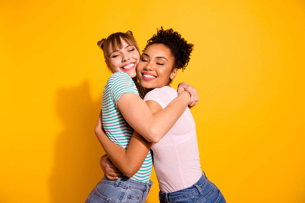 Portrait of charming cute pretty ladies cuddle tender gentle positive bun close eyes wear modern trendy style stylish t-shirt jeans wavy curly hairdo isolated on yellow background - 写真・画像