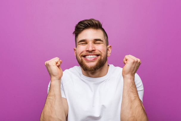 Young handsome caucasian man raising fist, feeling happy and successful. Victory concept. - Fotoğraf, Görsel
