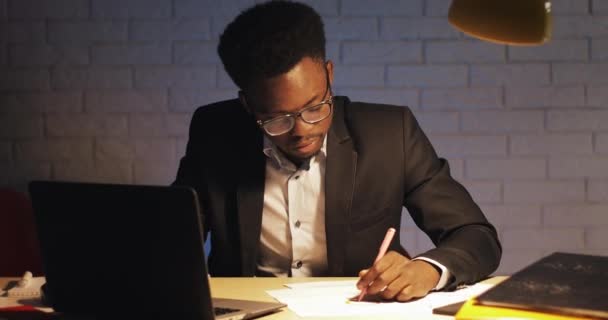 Tired businessman with laptop computer and papers working at night office. He signs the documents. Workaholic, deadline concept. Stressed businessman with headache working late at his office. - Кадры, видео
