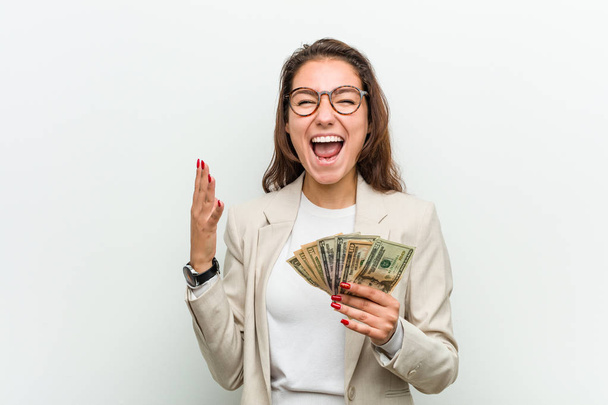 Young european business woman holding dollar banknotes celebrating a victory or success - Photo, Image