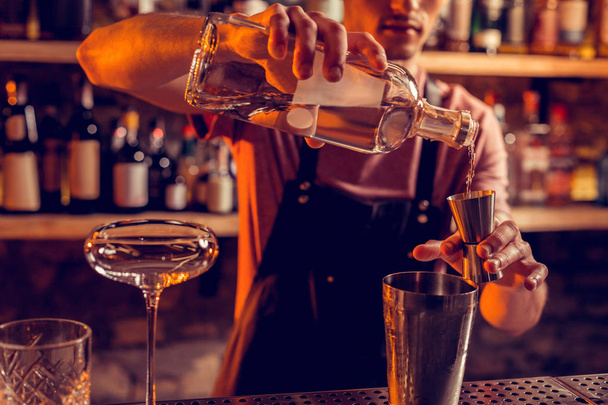 Barman vistiendo delantal negro vertiendo vodka para cóctel
 - Foto, imagen