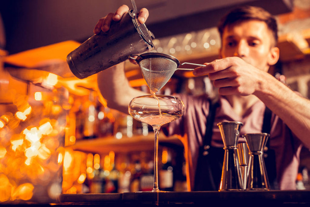 Barman aux cheveux bruns utilisant un tamis tout en faisant un cocktail
 - Photo, image