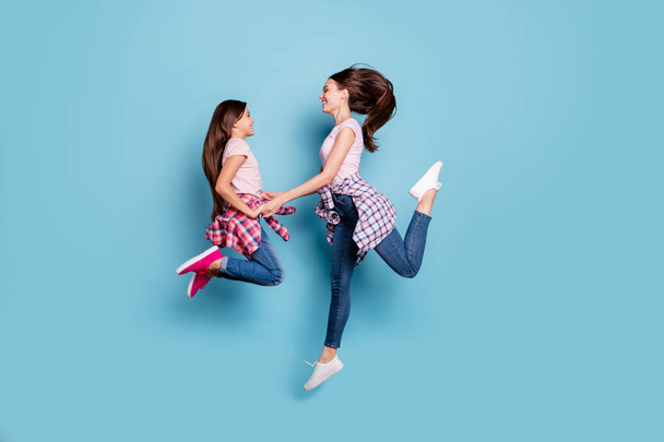 Full length body size profile side view portrait of two nice attractive cheerful cheery friendly straight-haired girls having fun holding hands isolated on bright vivid shine blue turquoise background - Photo, image