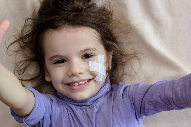 Little girl with adhesive plaster on face making selfie. - Valokuva, kuva