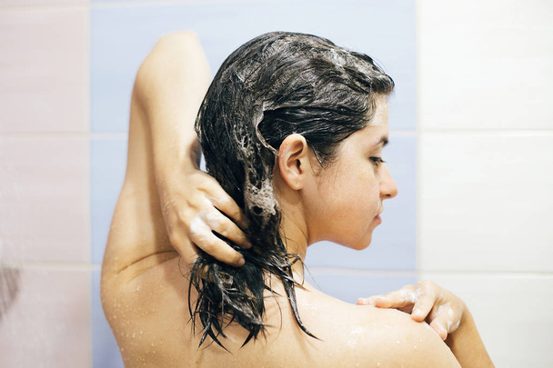 Nuori onnellinen nainen pesee hiuksensa shampoolla, vaahtoaa ha
 - Valokuva, kuva