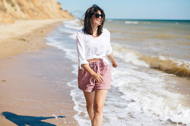 Happy young boho woman running and smiling in sea waves in sunny - Photo, Image