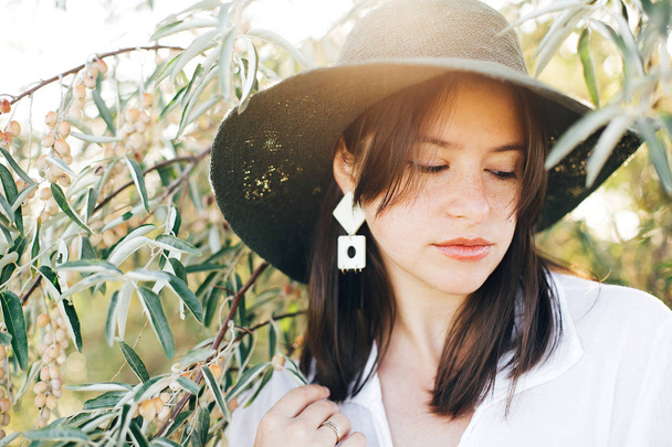 Stylish boho girl in hat and with modern earrings posing among g - Foto, imagen