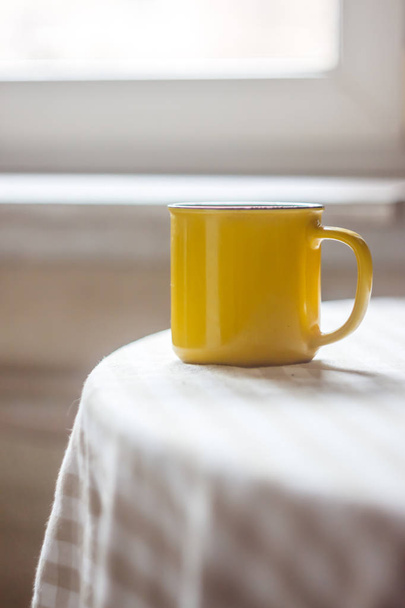 Uma xícara amarela de chá de café fica em uma mesa brilhante no ensolarado
 - Foto, Imagem
