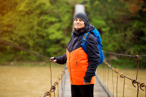 Portret van senior vrouw met rugzak op wandeling Cross River in bos - Foto, afbeelding
