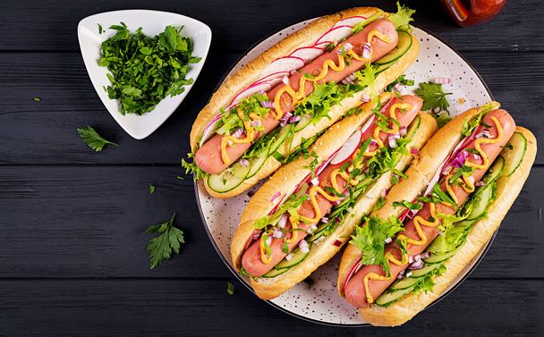 Hotdog met worst, komkommer, radijs en sla op donkere houten achtergrond. Zomer hotdog. Top View - Foto, afbeelding