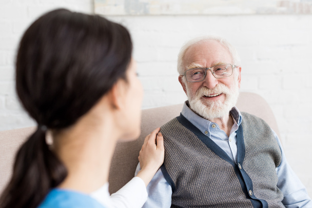 Selective focus of smiling grey haired man looking at nurse - Photo, Image
