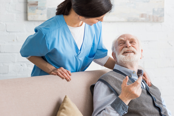 Heureux homme âgé regardant infirmière, assis sur le canapé
 - Photo, image