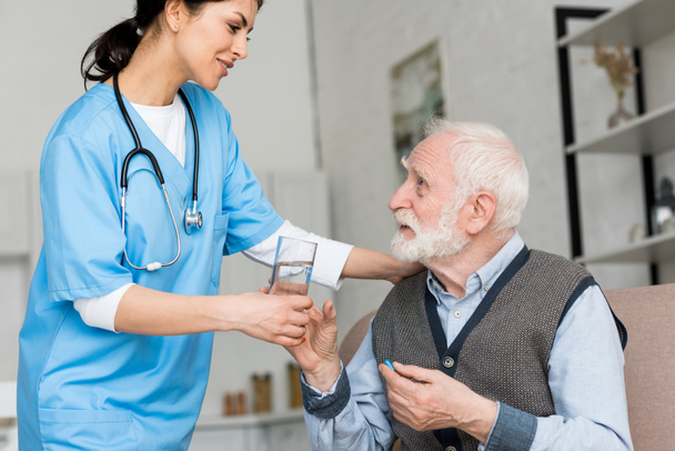 Nurse giving glass of water to elderly man with pill in hand - 写真・画像