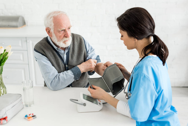Медсестра вимірює кров'яний тиск бородатого сірого волосатого чоловіка
 - Фото, зображення