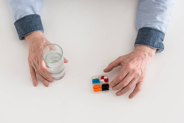 Cropped view of senior man holding glass with water and pills in hands - 写真・画像