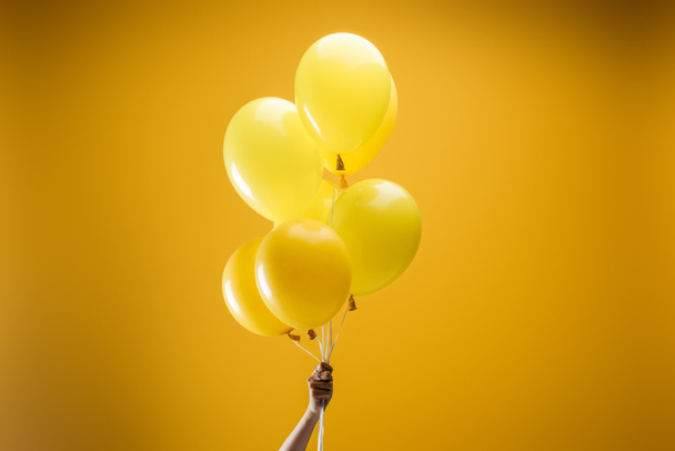 cropped view of woman holding festive bright minimalistic decorative balloons on yellow background - Фото, зображення