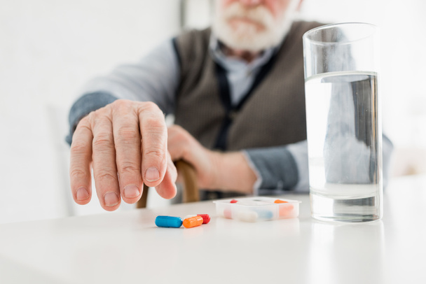 Cropped view of senior man picking up pills from table - 写真・画像