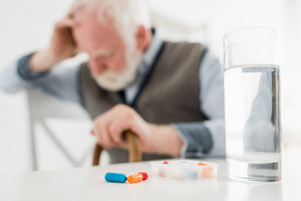 Selective focus of pills and water in glass on sad senior man background - Фото, зображення