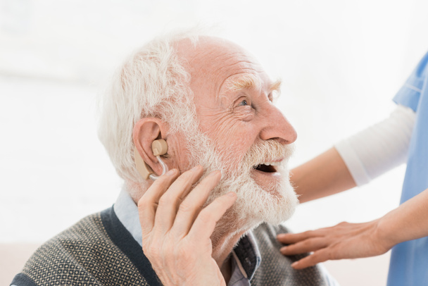 Профиль счастливого и веселого человека со слуховым аппаратом в ухе, отворачивающегося
 - Фото, изображение