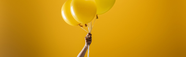 cropped view of woman holding festive bright minimalistic decorative balloons on yellow background, panoramic shot - Zdjęcie, obraz