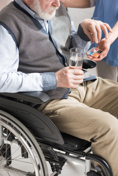 Vista recortada del médico dando pastillas al hombre mayor discapacitado en silla de ruedas
 - Foto, Imagen