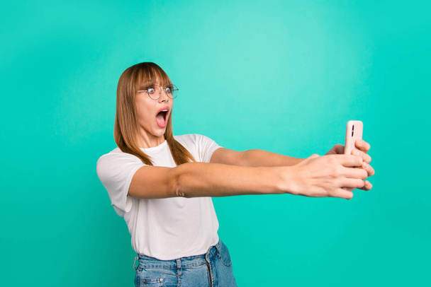 Close up photo amazing beautiful she her lady arm hand hold telephone make take selfies speak tell skype listening unbelievable news wear specs casual white t-shirt isolated teal green background - Zdjęcie, obraz