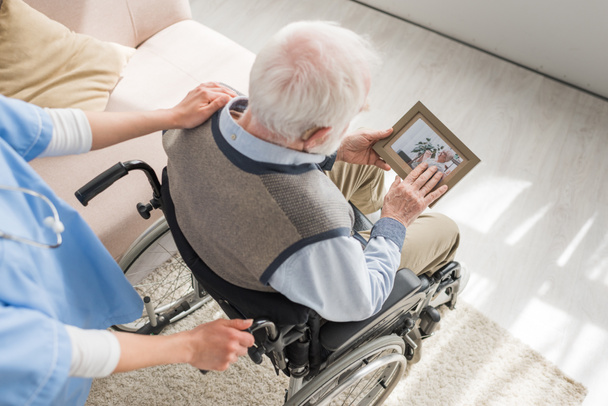 Высокий угол обзора медсестры, стоящей позади инвалида седой мужчина в инвалидной коляске
  - Фото, изображение