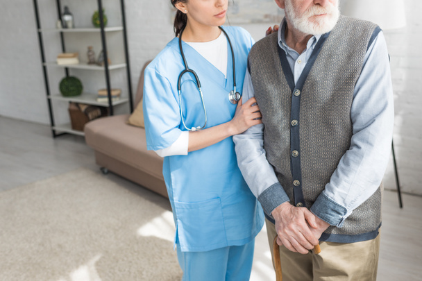 Vista recortada del hombre de pelo gris de pie con la enfermera en habitación luminosa
 - Foto, Imagen