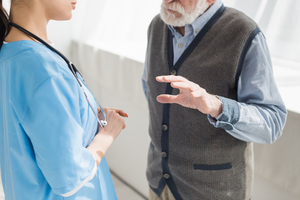 Ausgeschnittene Ansicht eines Rentners, der gestikuliert und mit einer Krankenschwester spricht - Foto, Bild
