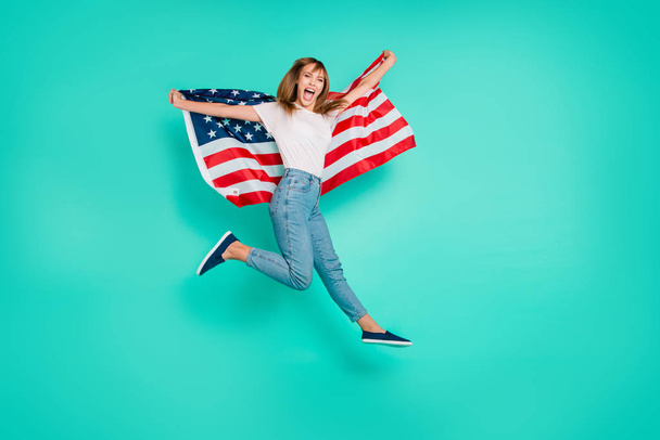 Full length side profile body size photo beautiful she her lady jump high arms hands hold american flag festive crazy carefree patriot wear specs casual white t-shirt isolated teal green background - Foto, immagini