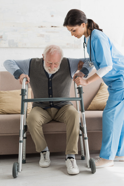 Nurse helping to retired man, getting up from sofa - Foto, imagen