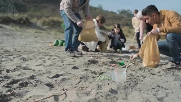 Plastic bekers en rietjes op het strand en de groep van vrijwilligers schoonmaken - Video