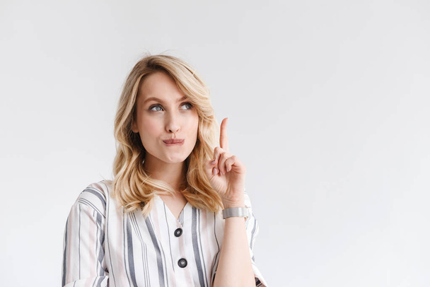Portrait of young blond woman wearing casual clothes looking at copyspace and pointing finger upward - Foto, Bild